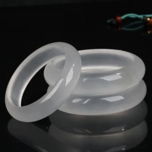 Multiple translucent white golden silk jade bangles displayed in three-quarter view on dark reflective studio background, showcasing smooth polished finish