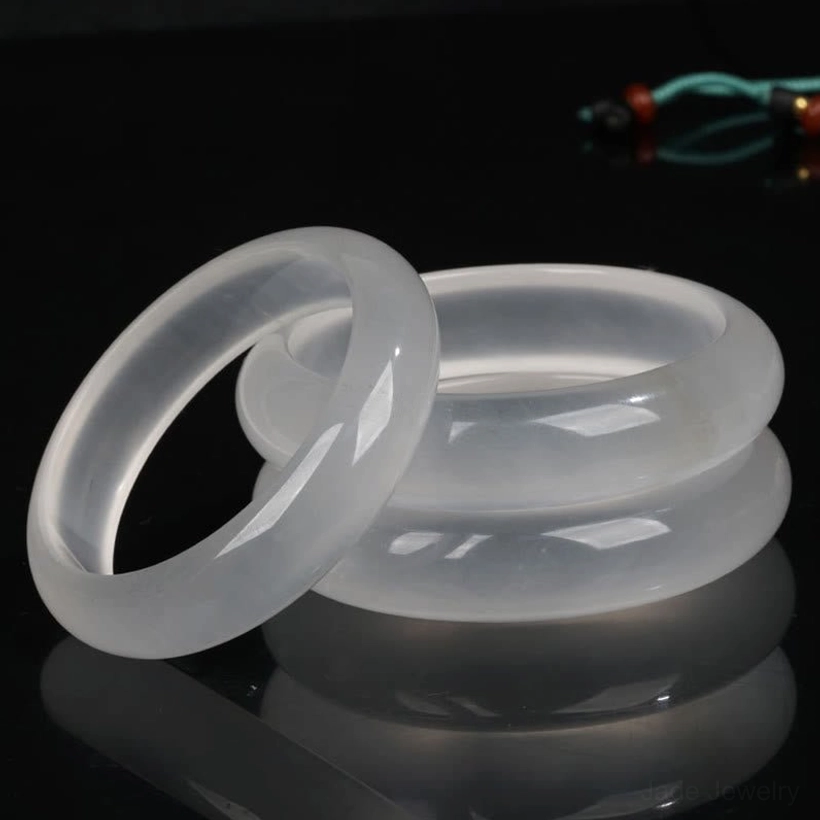 Multiple translucent white golden silk jade bangles displayed in three-quarter view on dark reflective studio background, showcasing smooth polished finish