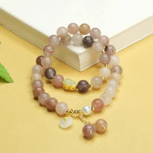 Double layer jade luck bracelet side view with book prop showing mixed tone golden silk jade beads and peace buckle charm detail