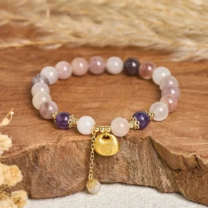 Golden silk jade Fu character blessing bracelet with gold charm and tassel, overhead flat lay view on wooden base with dried flowers