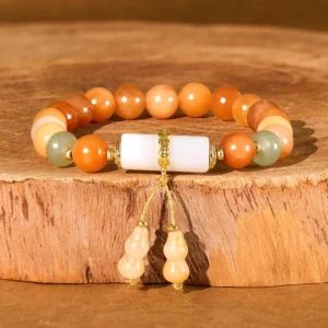 Golden Silk Jade white crystal gourd charm bracelet flat lay on wooden base, warm orange jade beads with white cylindrical charm