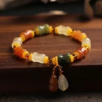 Golden Silk Jade Gourd Charm Bracelet - Multi-stone beaded design with dual drop pendants on dark wooden surface