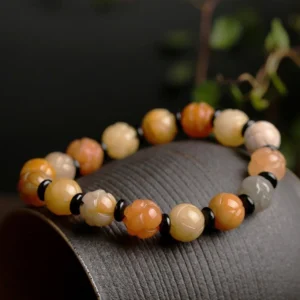 Golden silk jade beaded bracelet side angled view on dark fabric, showing mixed warm jade hues and intricately carved lotus beads