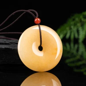 Yellow golden jade peace buckle pendant three-quarter angle view with brown wax cord and red bead