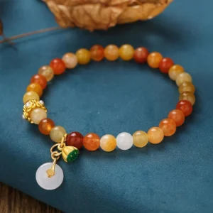Handcrafted golden silk jade beaded bracelet featuring amber-red gradient beads, decorative gold clasp, and peace buckle pendant on blue fabric