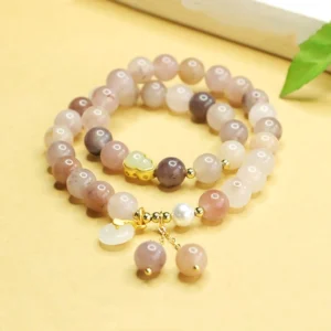 Golden Silk Jade double layer peace buckle bracelet overhead flat lay with jade beads, gold spacer details, and dangling charm on warm desktop