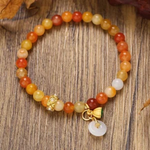Golden silk jade peace buckle bracelet with warm gradient beads and gold-toned peace buckle charm on wooden surface