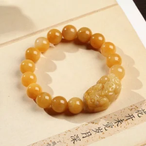 Overhead view of Golden Silk Jade Pixiu Bracelet displaying detailed carved Pixiu ornament and uniform yellow jade beads on antique paper background