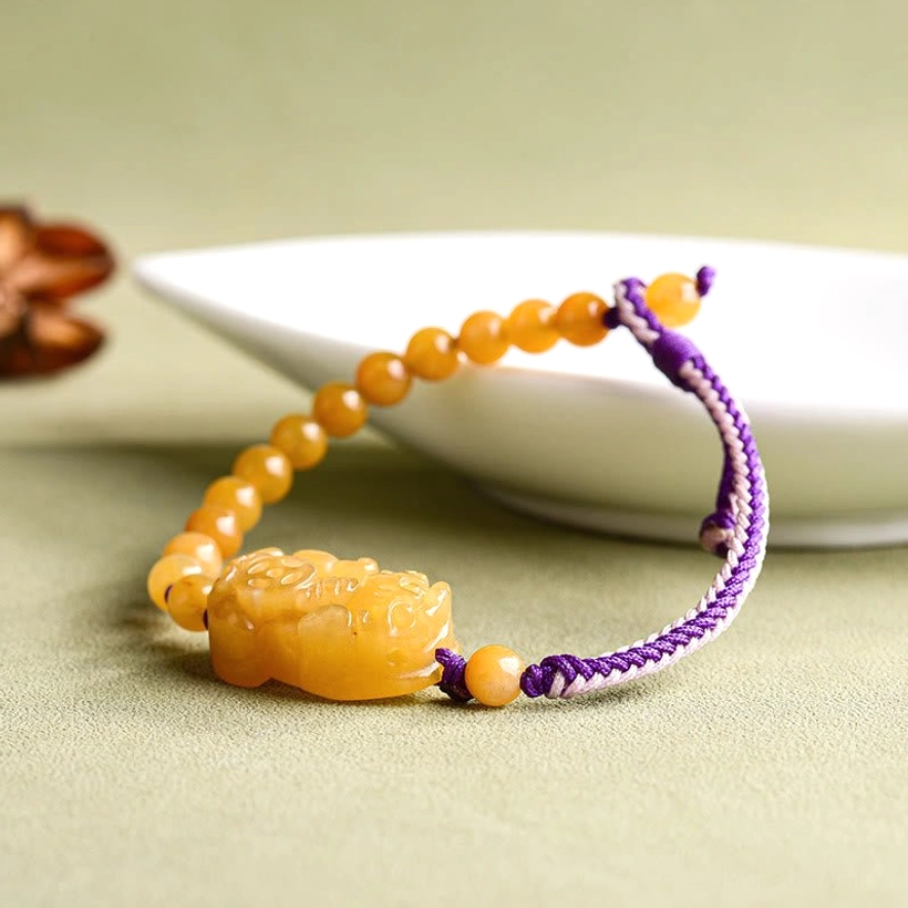 Golden Silk Jade Pi Xiu prosperity bracelet overhead side view on white plate with green background
