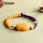 Golden Silk Jade Pi Xiu wealth bracelet close-up side view with purple adjustable cord and carved charm