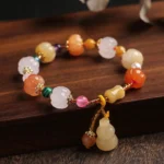 Golden silk jade pixiu gourd bracelet overhead flat lay on dark wood showing warm toned gem beads