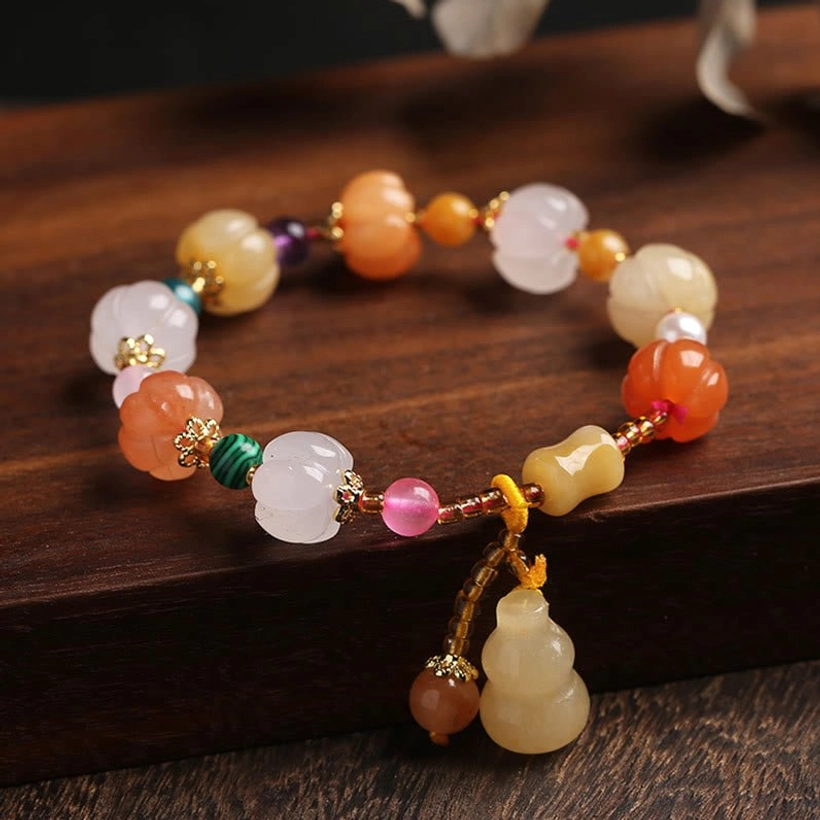 Golden silk jade pixiu gourd bracelet overhead flat lay on dark wood showing warm toned gem beads