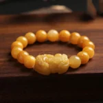 Golden Silk Jade Pixiu Wealth Bracelet with carved Pixiu charm, featuring warm yellow jade beads arranged on dark wooden surface
