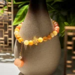 Golden Silk Jade pumpkin wealth bracelet with Chinese knot displayed on ceramic vase with oriental decor