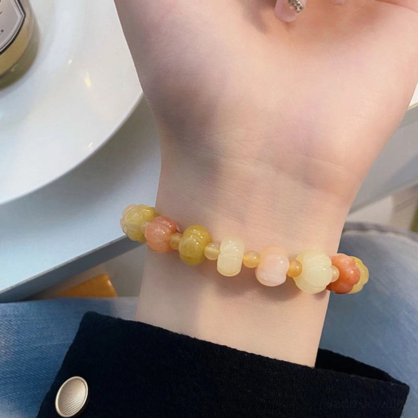 Golden Silk Jade pumpkin bracelet worn on wrist with white tabletop background showing mixed warm toned beads
