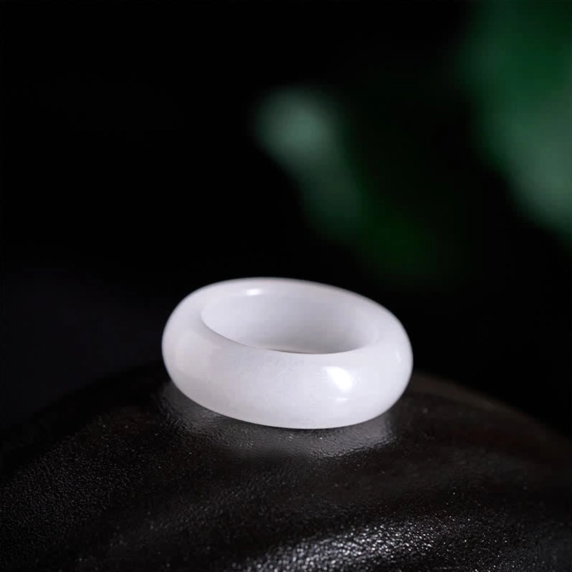 Pale white golden silk jade ring flat lay on black glossy surface showing soft muted finish and rounded band