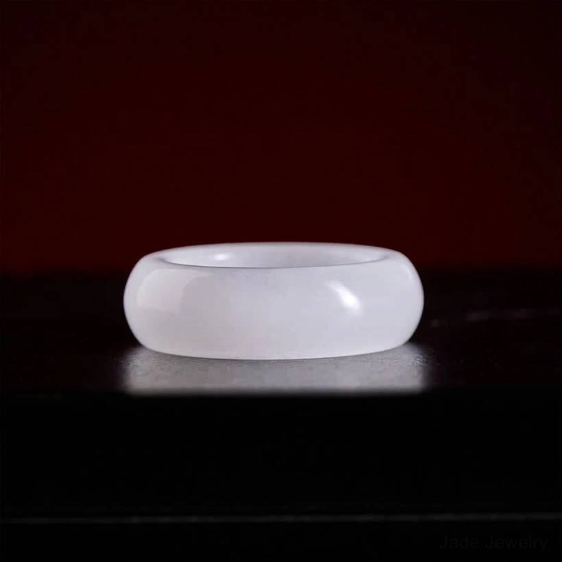 Light muted golden silk jade ring on dark reflective surface showcasing smooth polished plain band design