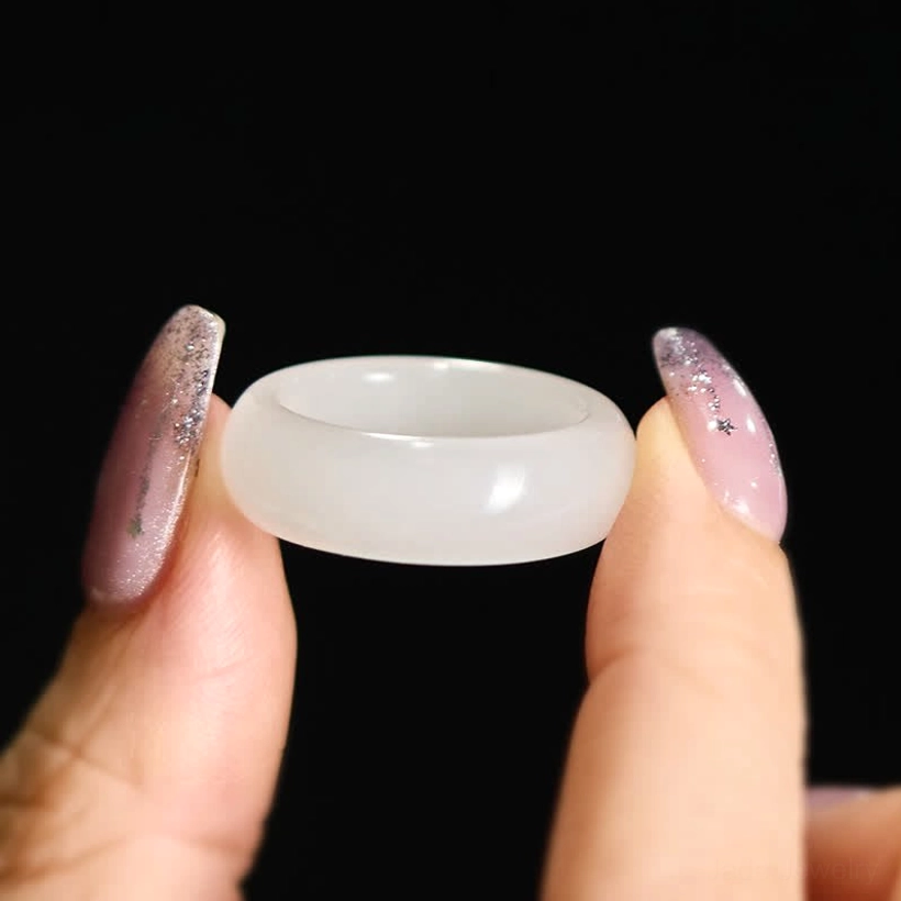Natural golden silk jade ring held between fingertips and decorative nails against dark background for scale reference