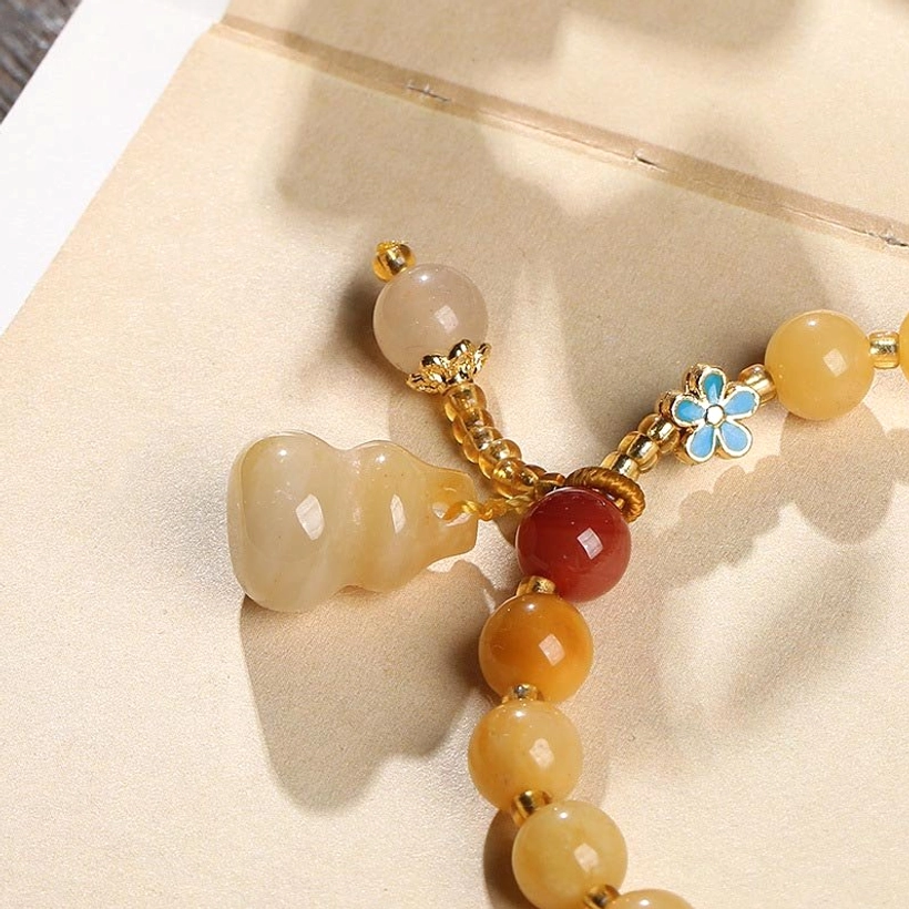 Close-Up of Gourd Pendant with Enamel Flower Detail on Golden Jade Bracelet