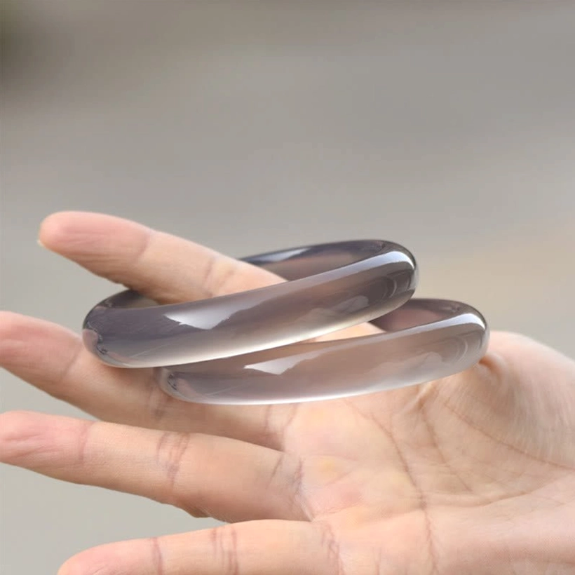 Two gray chalcedony bangle bracelets stacked parallel on palm, overhead view displaying smooth polished surface