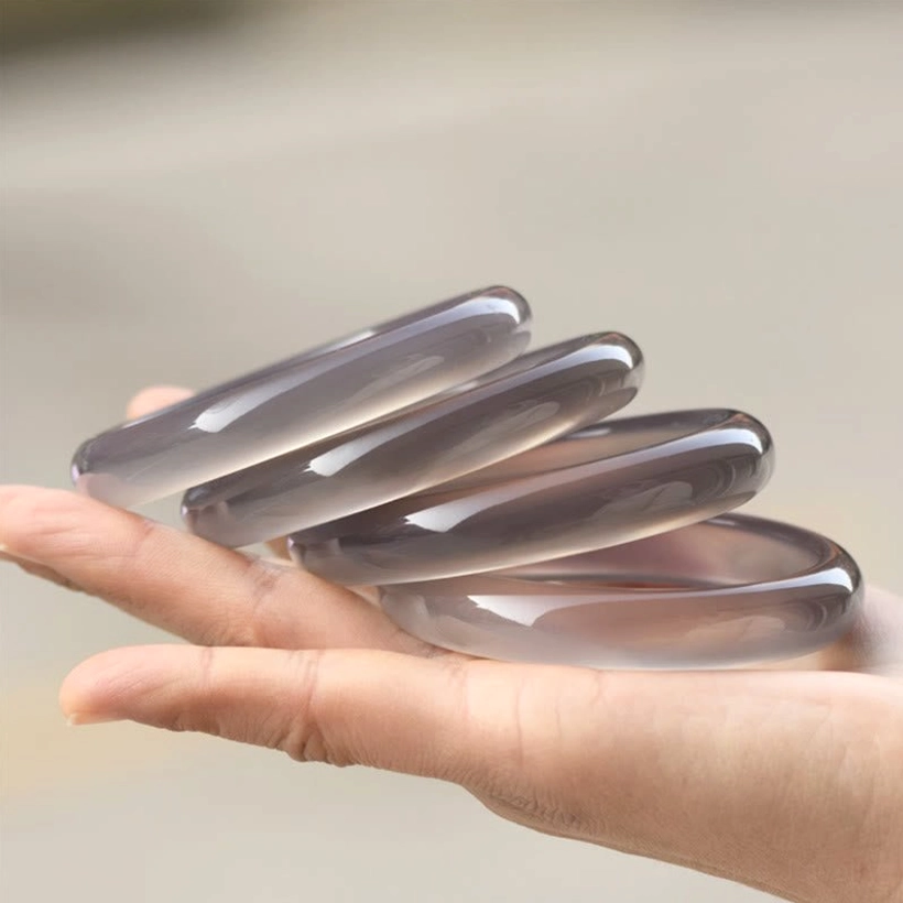 Four gray chalcedony bangle bracelets fanned and stacked on palm, showing polished surface quality and variety of sizes