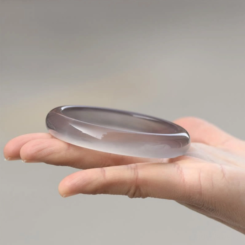 Single gray chalcedony bangle bracelet held in palm, side view showcasing glossy polish and elegant minimalist design