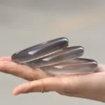 Three stacked gray chalcedony bangle bracelets displayed on palm, showing translucent polished stone finish and smooth rounded bands