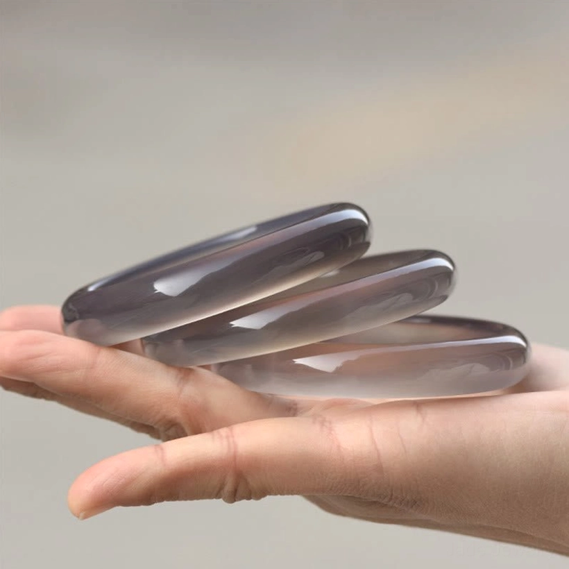 Three stacked gray chalcedony bangle bracelets displayed on palm, showing translucent polished stone finish and smooth rounded bands