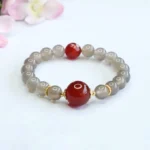 Gray chalcedony and red agate beaded harmony bracelet with gold spacers displayed on white background with pink flowers