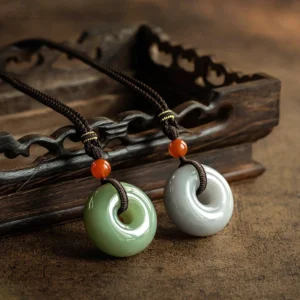 Two gray jade peace buckle pendants with braided decorative cords on carved wooden surface