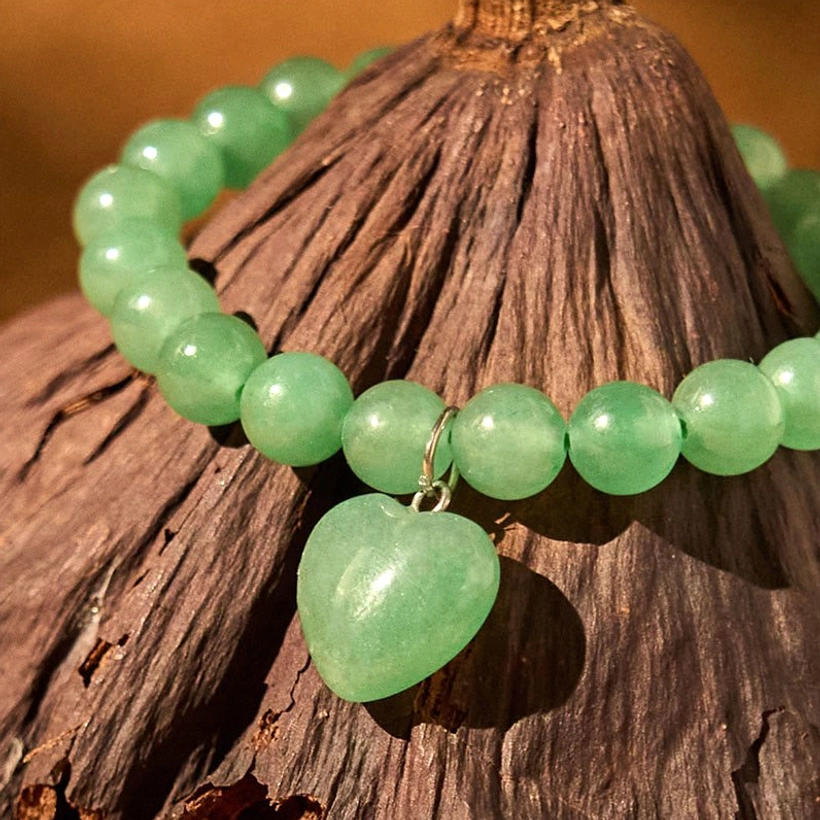 Natural stone heart bracelet with round green aventurine beads and dangling heart pendant on textured background