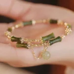 Green bamboo jade bangle bracelet held in palm, displaying carved bamboo pattern jade segments, gold chain details, and delicate jade tassel pendant