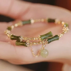 Green bamboo jade bangle bracelet held in palm, displaying carved bamboo pattern jade segments, gold chain details, and delicate jade tassel pendant