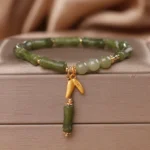 Green bamboo jade wealth bracelet with gold bamboo charm on luxury satin jewelry box