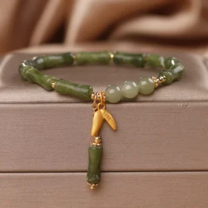 Green bamboo jade wealth bracelet with gold bamboo charm on luxury satin jewelry box