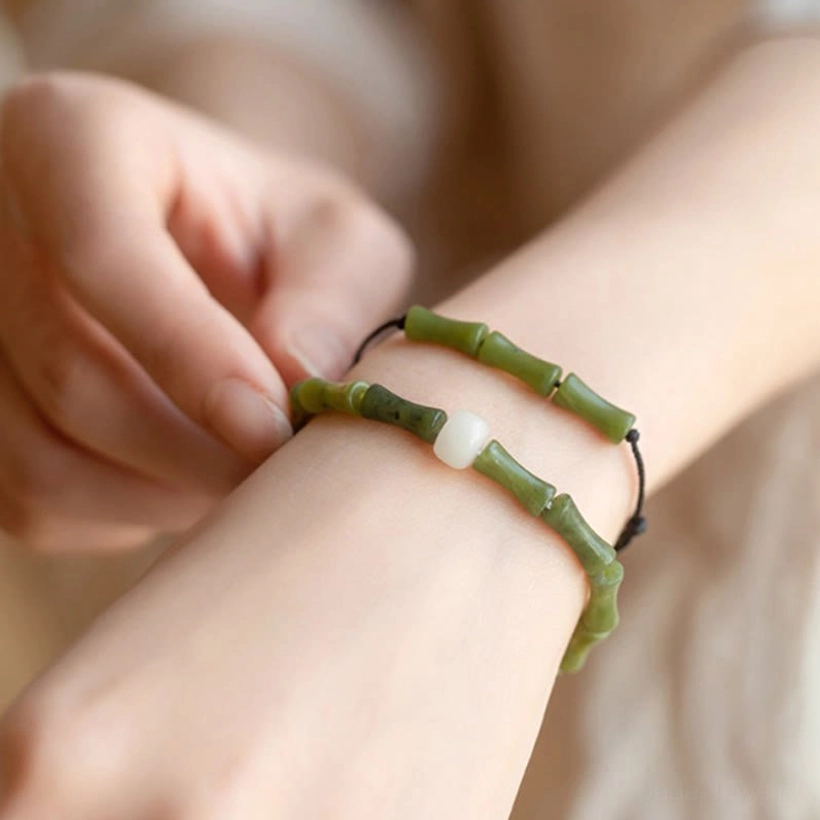 Green bamboo jade bracelet worn on wrist, close-up lifestyle shot showing carved bamboo beads with white jade accent
