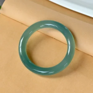 Natural green chalcedony bangle with deep aqua green tone, angled view on kraft paper background showing smooth polished surface