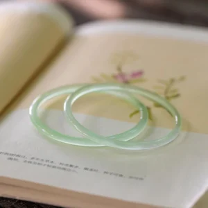 Pair of light green chalcedony polished bangles arranged on vintage book, soft seafoam finish, slender 4mm width