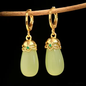 Green chalcedony jade earrings hanging on wooden branch with floral metal cap details and small green stone accents minimalist styling
