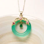 Green chalcedony peace buckle pendant with gold filigree frame and pink gem accents on ceramic dish