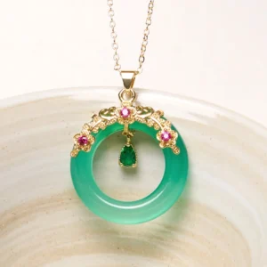 Green chalcedony peace buckle pendant with gold filigree frame and pink gem accents on ceramic dish