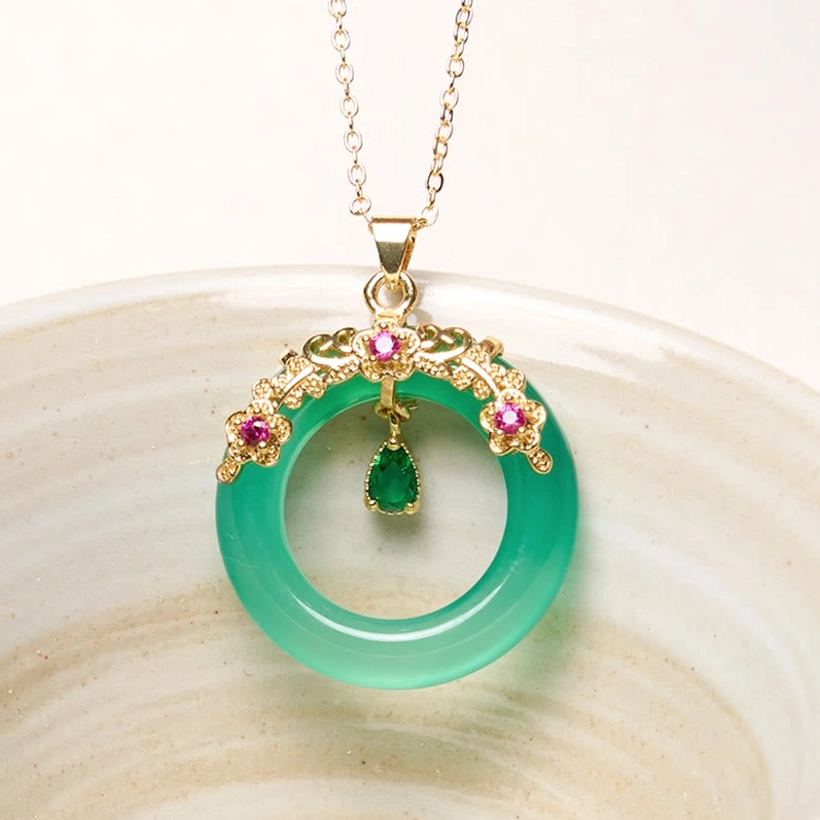 Green chalcedony peace buckle pendant with gold filigree frame and pink gem accents on ceramic dish