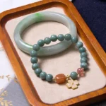 Green jade bangle and beaded jade bracelet set with strawberry quartz and gold four-leaf charm displayed on velvet tray - prosperity bundle