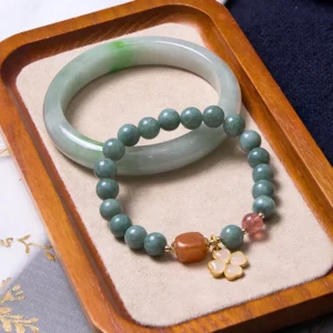 Green jade bangle and beaded jade bracelet set with strawberry quartz and gold four-leaf charm displayed on velvet tray - prosperity bundle