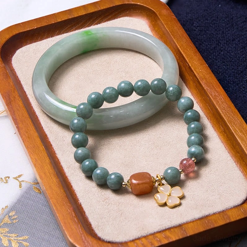 Green jade bangle and beaded jade bracelet set with strawberry quartz and gold four-leaf charm displayed on velvet tray - prosperity bundle