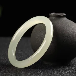 Pale green jade bangle three-quarter side view showing glossy polished round band with ceramic vase