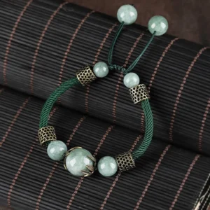 Green jade adjustable bracelet flat lay showing uniform jade beads and metal accents with pull-tie closure on dark fabric