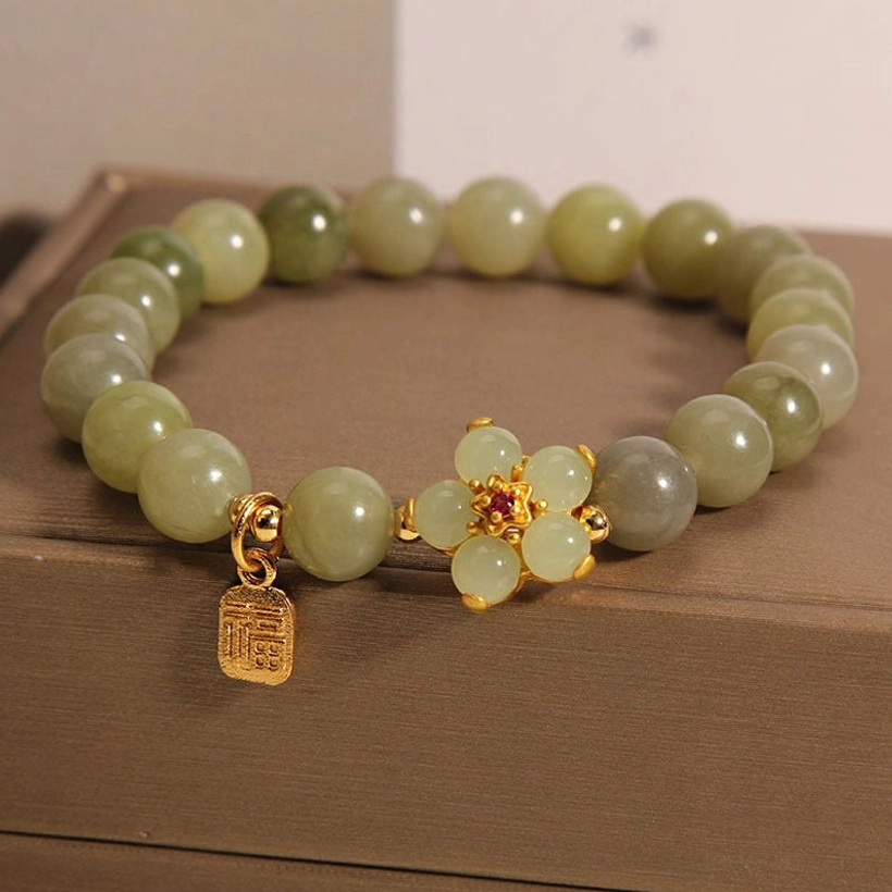Gold flower charm and Fu character pendant attached to green jade beaded bracelet showing craftsmanship details