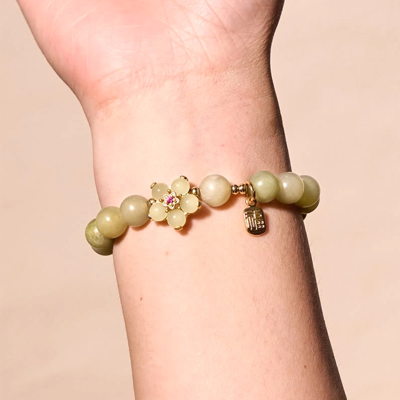 Green jade bracelet with Fu charm worn on wrist - front close-up showing two-tone jade beads, floral charm with red gem accent, and Fu character tag