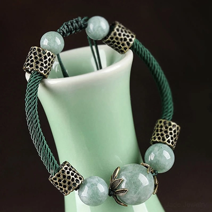 Green jade bracelet resting on celadon ceramic with lotus-shaped bead caps and mixed-size jade beads